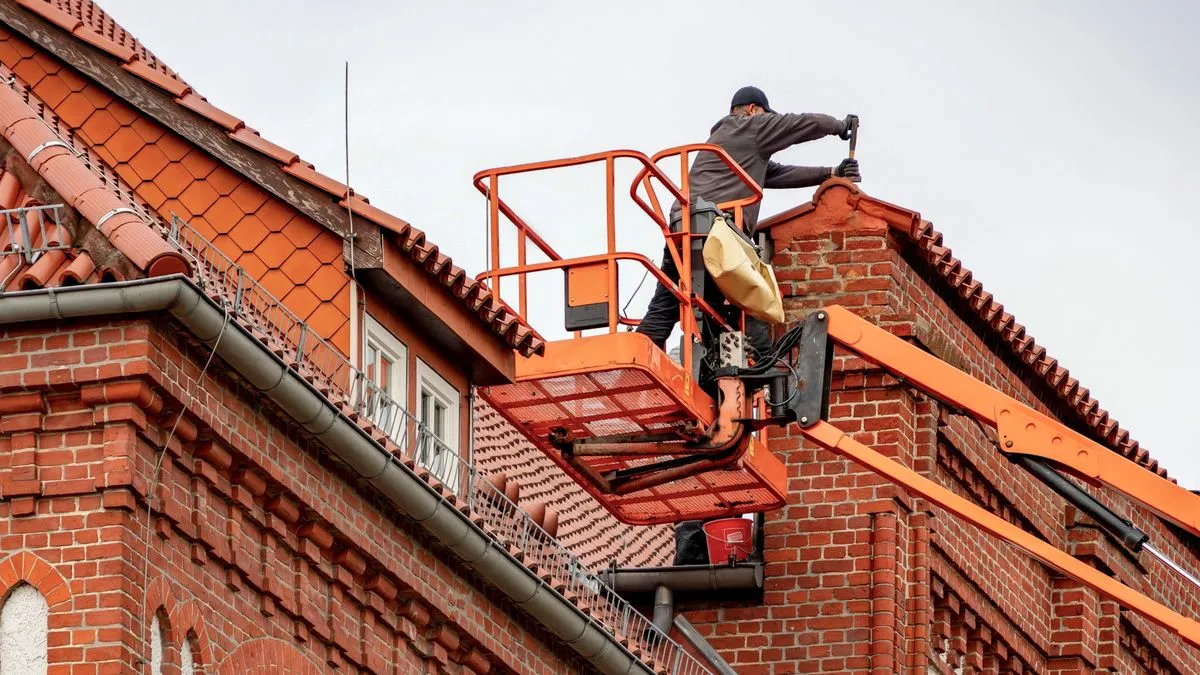 Handwerker auf einer Hebebühne arbeitet am Ziegeldach eines Backsteinhauses
